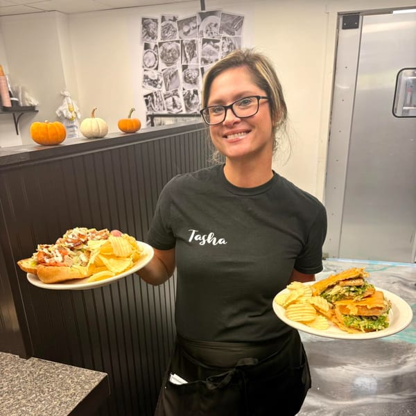 Smiling Annamarie's on Main staff member, Tasha, holding two plates with sandwiches and chips.